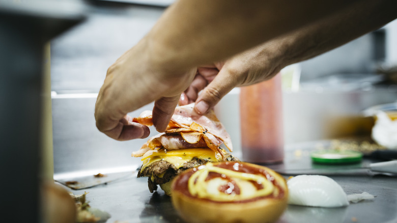 Man's hands assembling a hamburger on a professional grill