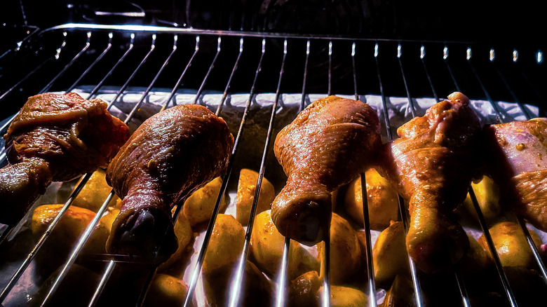 Chicken legs broiling on oven rack above sheet pan of potatoes