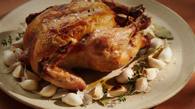 A roast chicken on a plate with roasted garlic