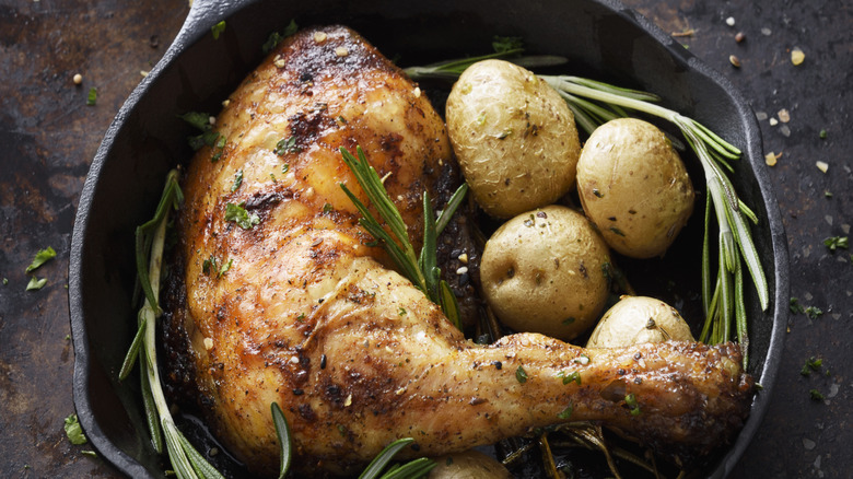 A chicken leg in a cast iron with potatoes and rosemary
