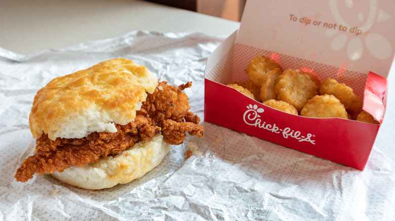 Chick-fil-A fried chicken biscuit next to red cardboard box of hash browns on paper wrapping
