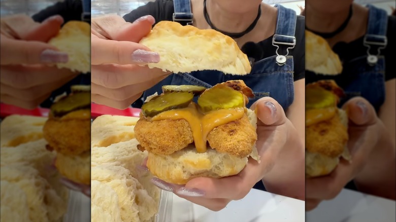 Person holding sandwich made with Costco Kirkland Signature biscuits, chicken strips, sauce, and pickle chips