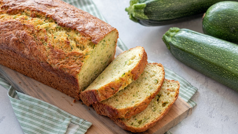 Top view of a partially sliced zucchini load alongside a fresh zucchini