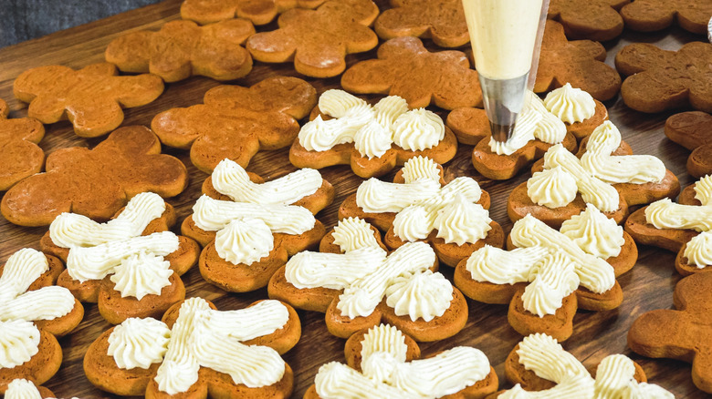 A person using a piping bag to add eggnog buttercream frosting to gingerbread sandwich cookies