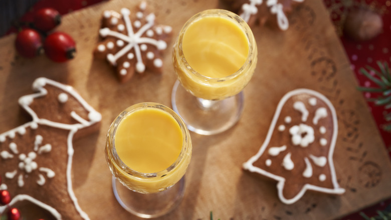 Two small glasses of eggnog on a table next to iced gingerbread cutout cookies