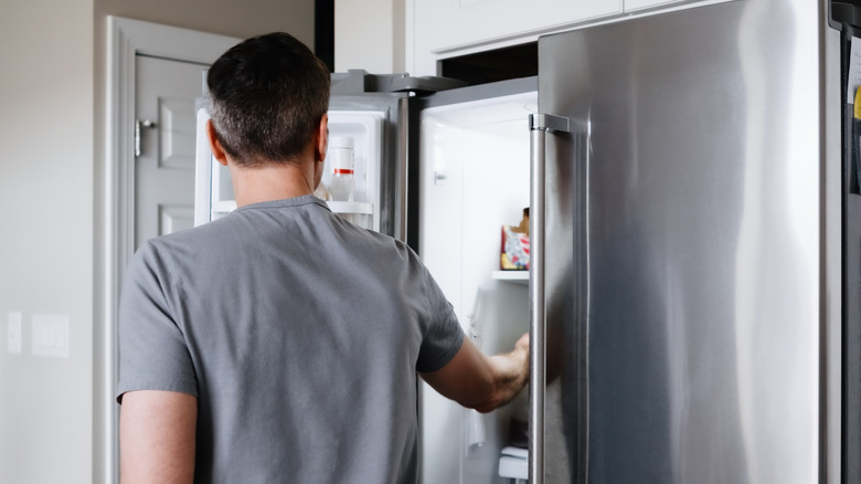 Man in grey t-shirt opens a French door fridge.