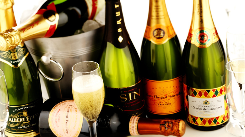 Various bottles of Champagne in a pile beside a flute of the drink