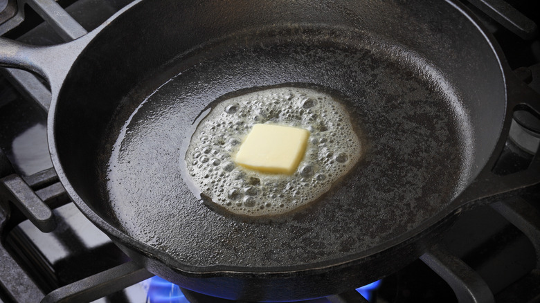 Cast iron frying pan with melting butter on a gas stove.