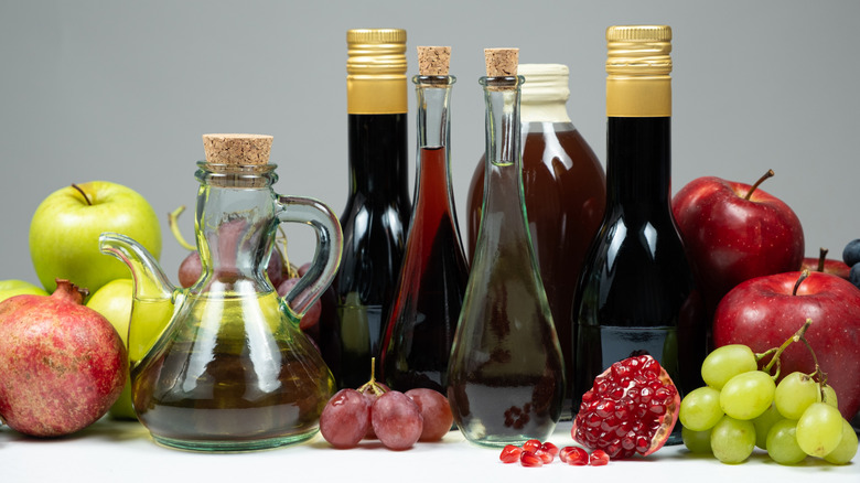 varieties of vinegar surrounded by apples, pomegranates, and grapes