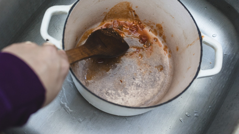 Scrubbing off sauce with wooden spoon from bottom of Dutch oven