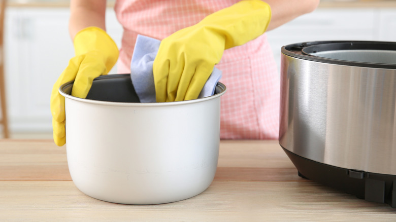 Closeup of person with gloves cleaning a slow cooker