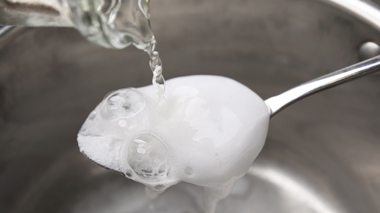 Closeup of pouring vinegar on spoon of baking soda