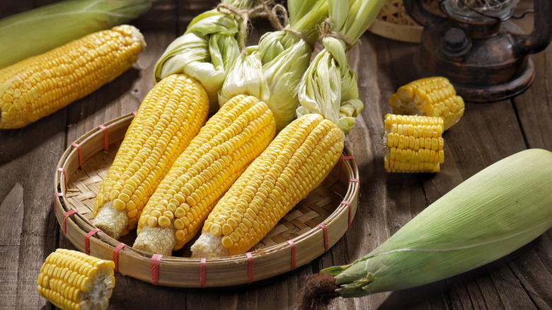 corn on the cob with pieces and husks in wicker bowl