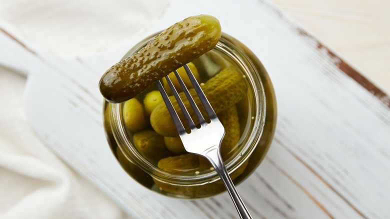 An overhead view of an open pickle jar with a fork spearing a pickle on top of the jar
