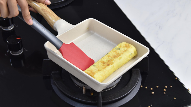 Hands cooking an omelette in a square pan with a red silicone spatula