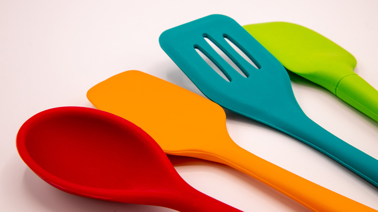 A lineup of four different silicone kitchen utensils in an array of bright colors
