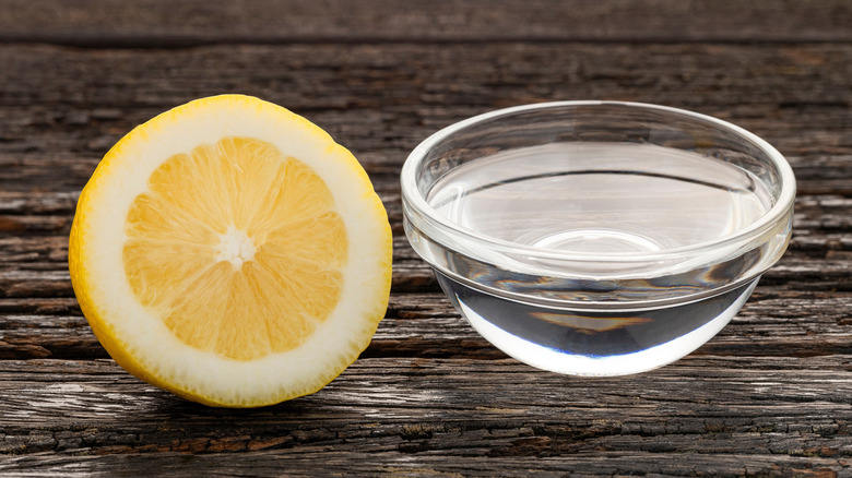 A small glass full of water next to a lemon cut in half