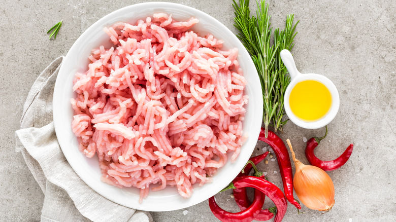 Raw ground turkey in white bowl with chicken stock, onions, rosemary, peppers