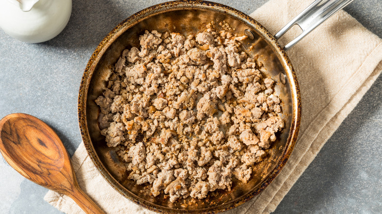 Sauté pan on napkin with ground turkey and wooden spoon