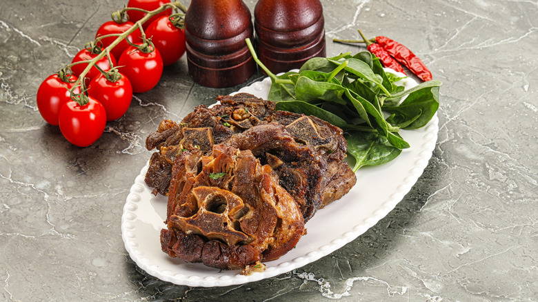 grilled lamb neck on a plate alongside basil, tomatoes and chilis