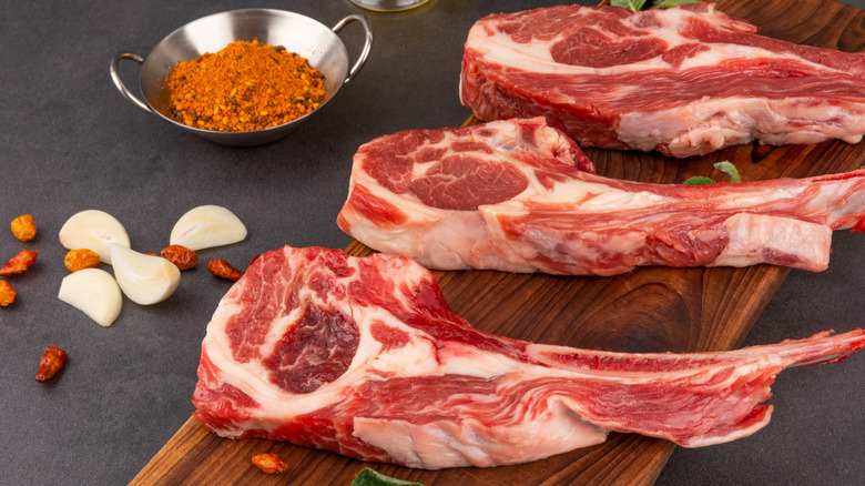 trimmed raw lamb chops on a cutting board next to spices and garlic