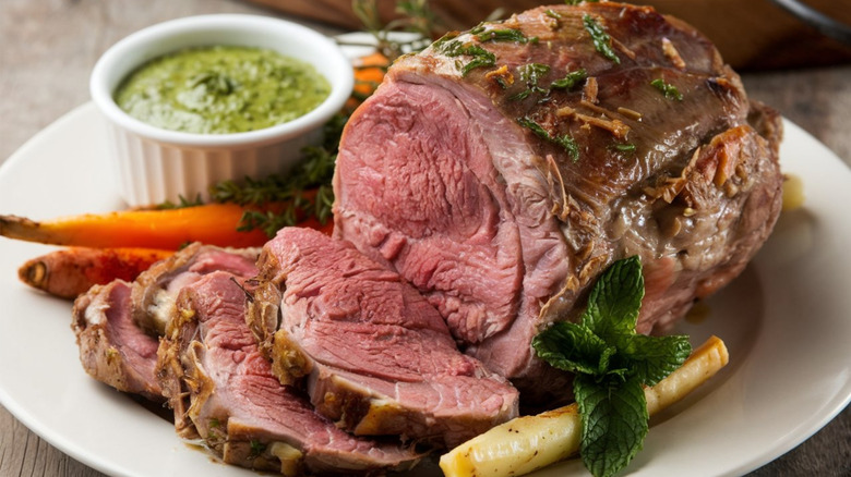 a sliced roast leg of lamb on a platter, garnished with herbs and carrots