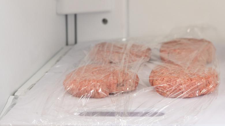 Beef patties covered in plastic wrap in a refrigerator