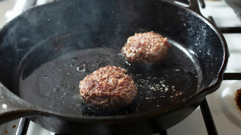Two beef patties cooking in a cast iron skillet