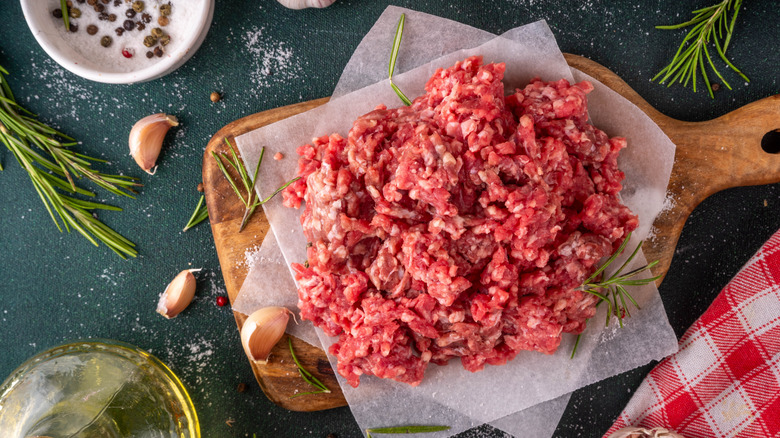 A pile of ground beef on a wooden cutting board surrounded by seasonings