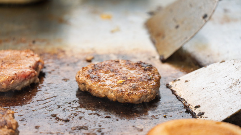 A burger on a flattop grill with metal spatulas