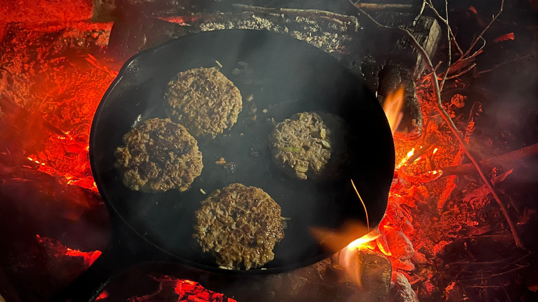 Burgers cooking in a cast iron skillet over open flames