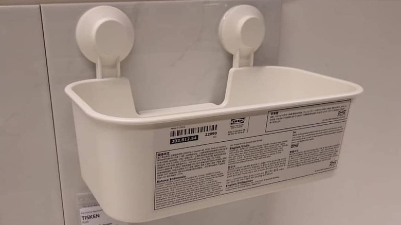 A white plastic IKEA TISKEN basket installed on a white tile wall