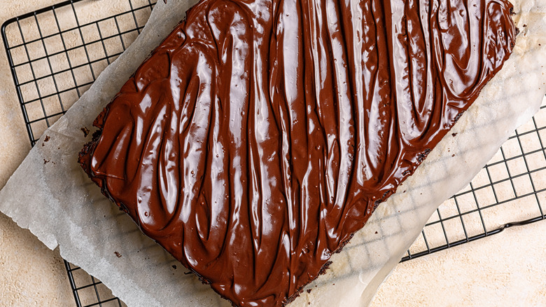 A chocolate frosted sheet cake, resting on a baking sheet on a wire rack
