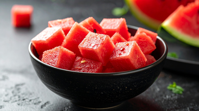Black bowl of watermelon cubes with a quartered melon in the background