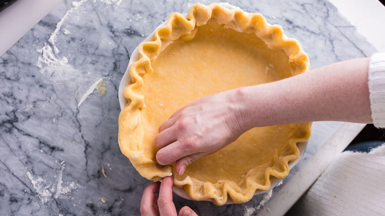Someone using their knuckles to make a pie crust in a glass pan
