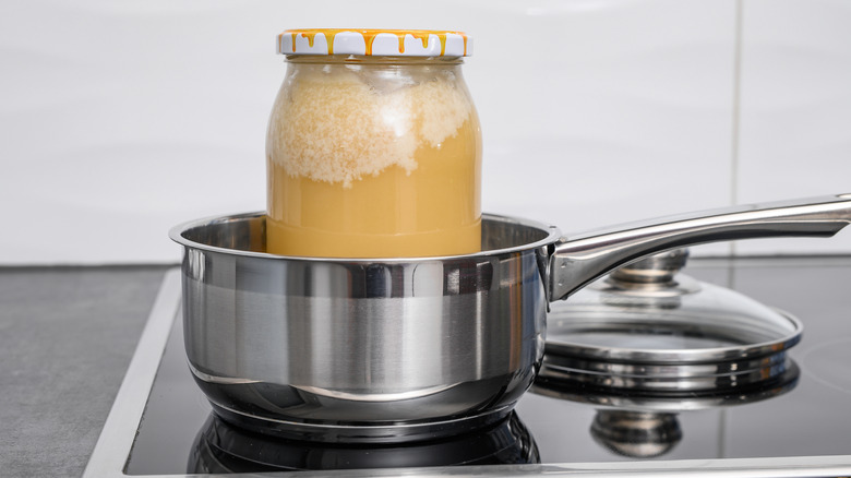 A glass jar of crystallized honey sitting in a stainless steel pot on a stovetop