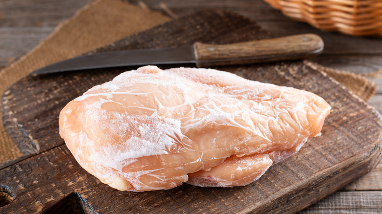 A large frozen chicken breast on a wooden cutting board next to a knife