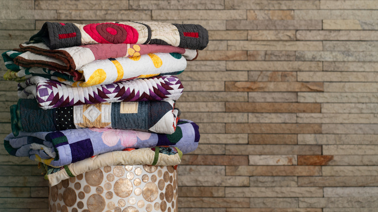 A pile of quilted fabrics placed on a bench against a brick wall