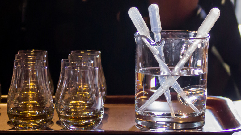 Two rows of whisky glasses containing Scotch on a tray, next to a beaker of water containing 3 pipettes