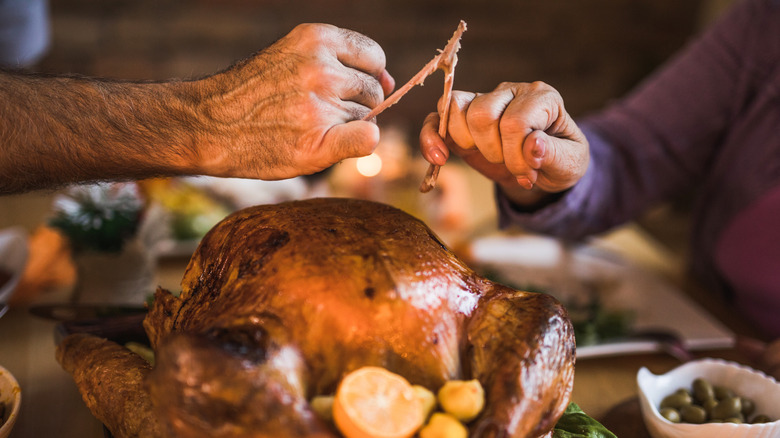 Two people splitting a wishbone over a turkey