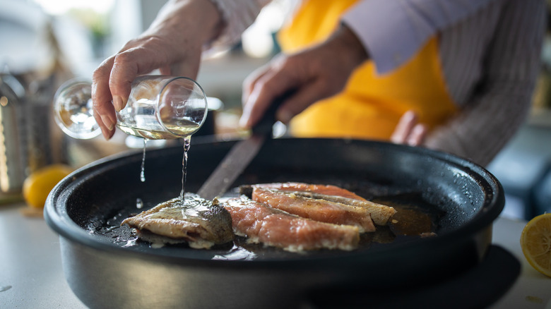 pouring sparkling wine into a pan of fish