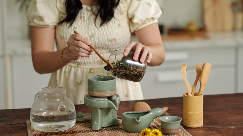 A woman in a white dress brewing green tea in her kitchen