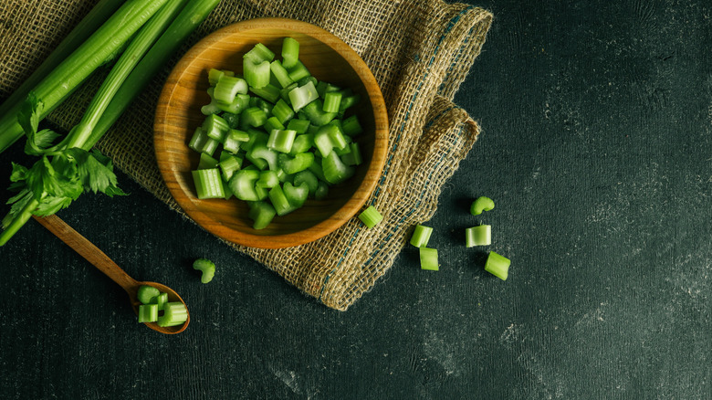 Chopped celery in bowl with stalks beside it