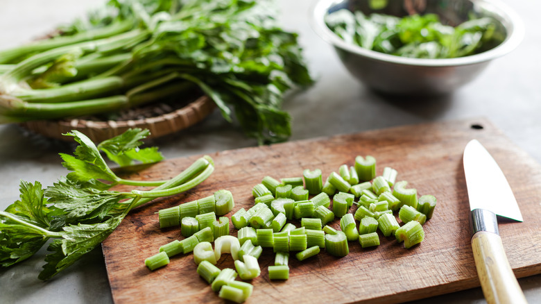 Celery stalks and chopped celery on cutting board with knife