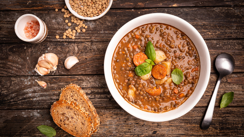 a bowl of brown lentil soup and sausage on a wooden background