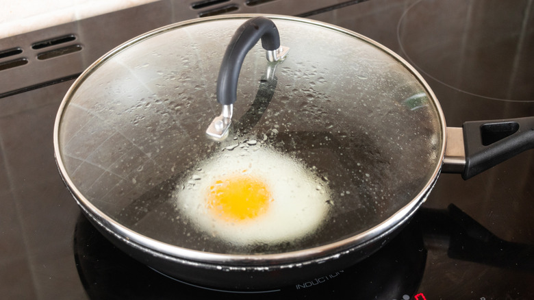 Egg cooking in frying pan with lid on