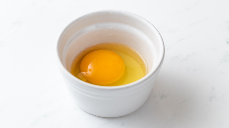 Egg cracked into small white bowl