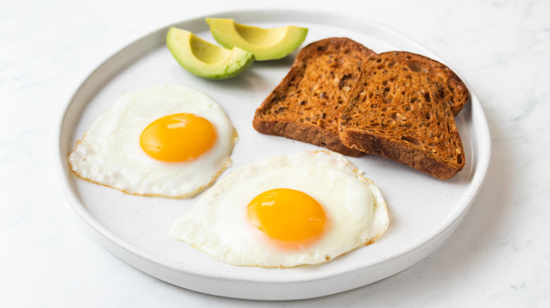 Two fried eggs on plate with toast and avocado