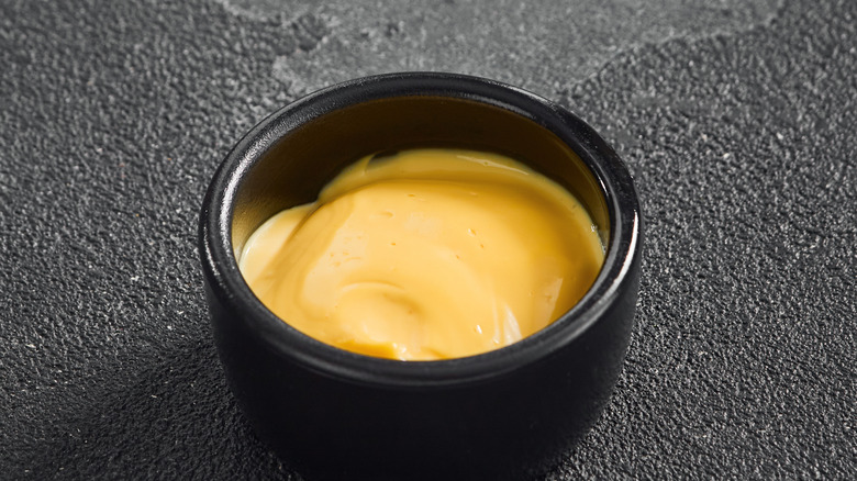 A cup of cheese sauce sits on a table.