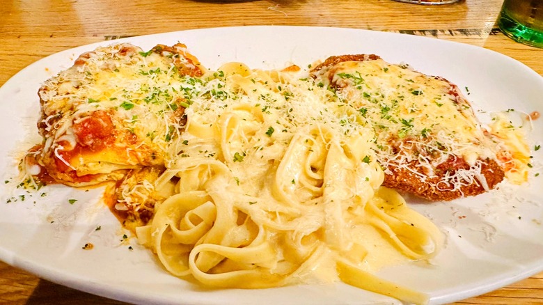 White plate of fettuccine Alfredo next to lasagna and chicken Parmigiana from Olive Garden